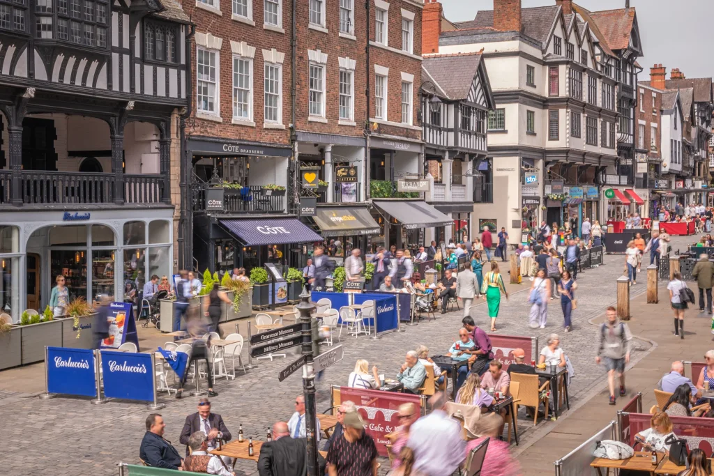 Bustling Bridge Street with people dining outdoors and historic timber-framed buildings in the background.