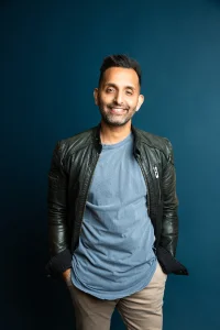 A photo of a man looking to camera in a blue top and leather jacket