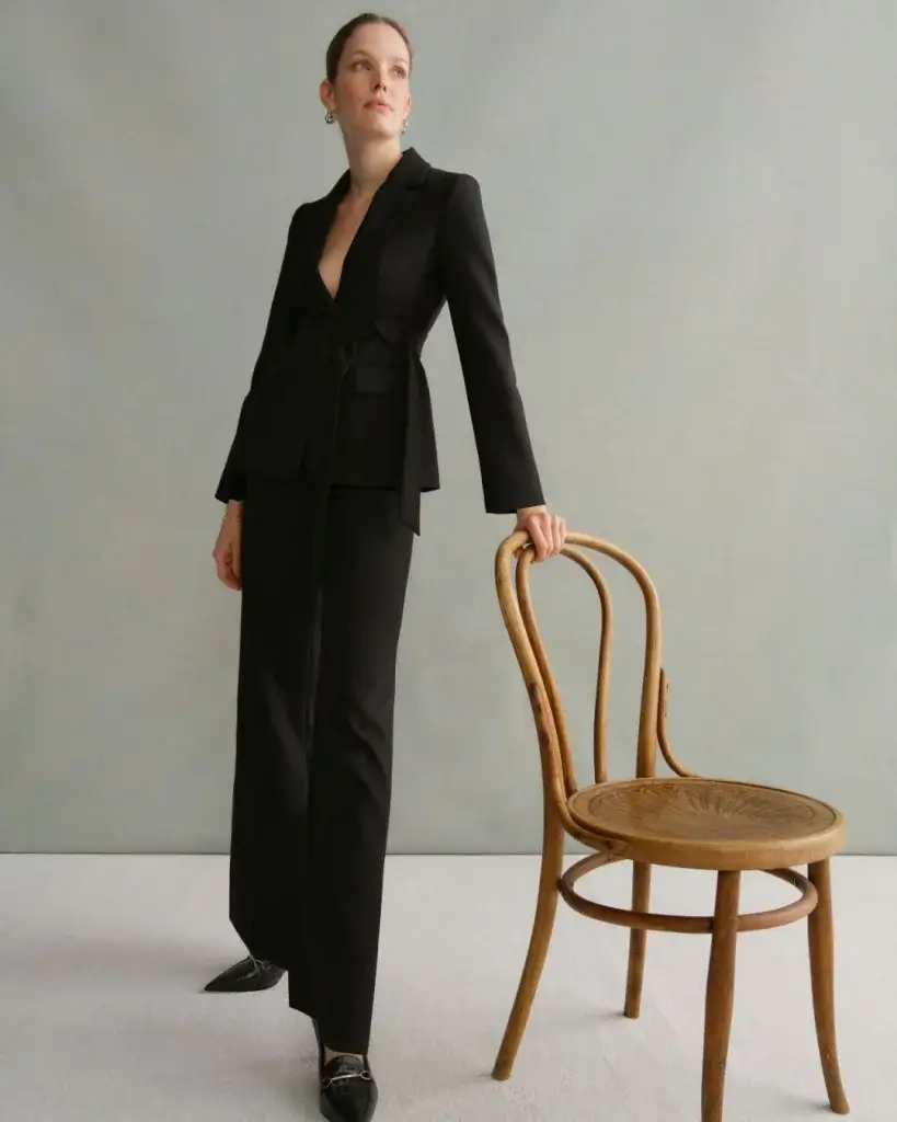 Female model wearing black standing with wooden chair