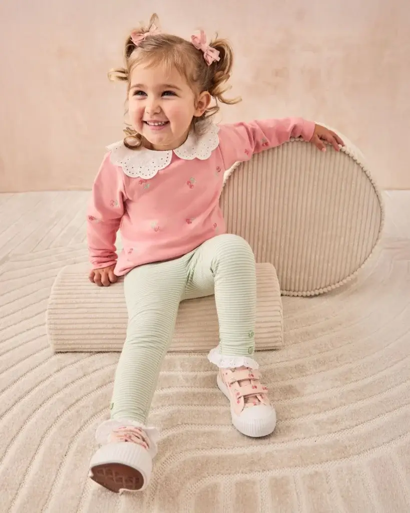 Young Girl smiling in pink and white trainers, white trousers and pink top with white colour