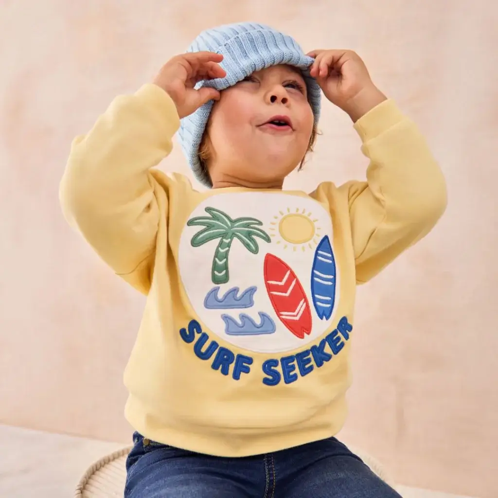 young boy in blue trainers, blue jeans, yellow jumper and light blue hat