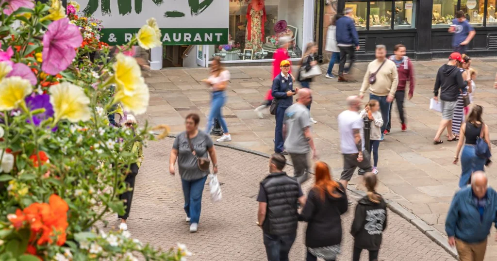 Chester BID City Host in Orange Hat standing on The Cross