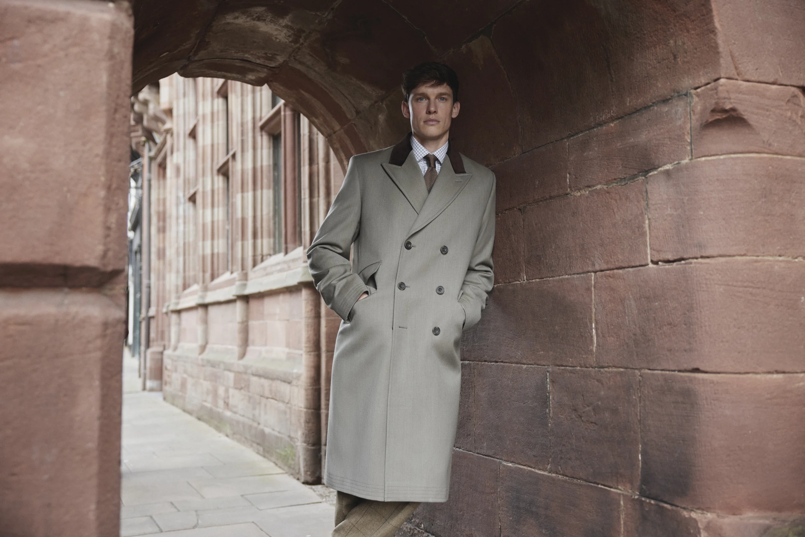 Male model standing underneath Eastgate Clock in Chester wearing a long grey coat