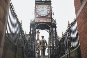 Male model standing underneath Eastgate Clock in Chester wearing a pale green/brown tweed suit