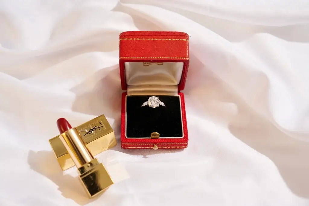 A vintage diamond ring in a red box on linen with YSL lipstick