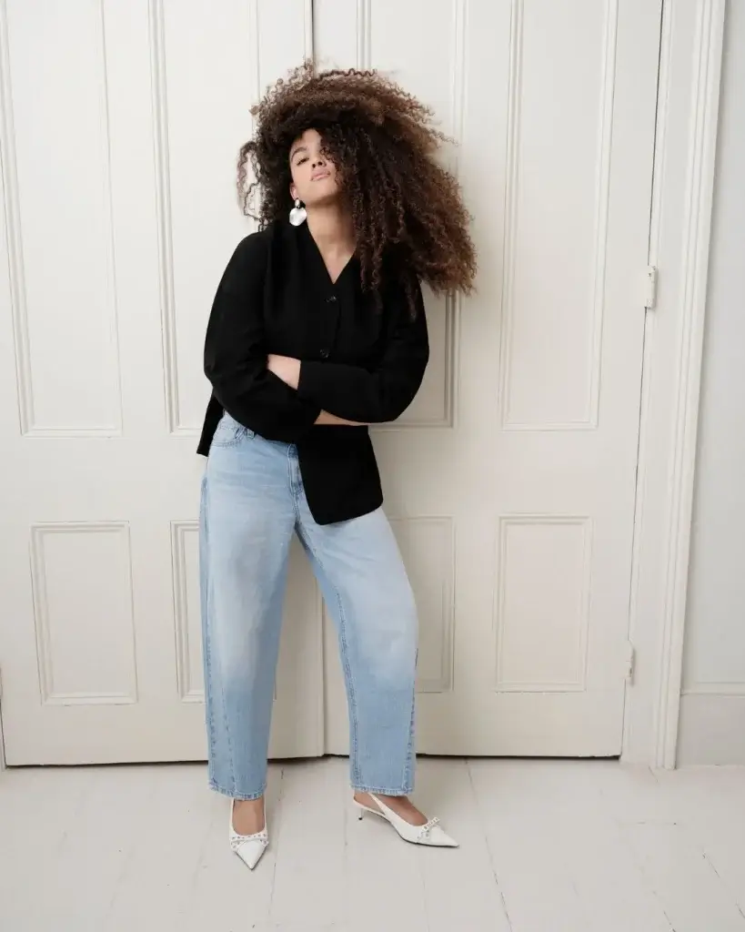 Woman with lots of hair in light blue denim jeans and a denim dark blue top in white high heels