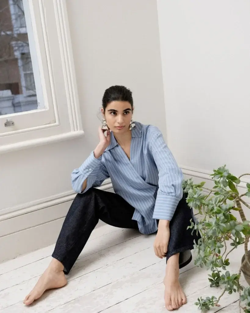 a woman with a light blue shirt bare foot in dark blue jeans sitting on white painted wooden floor