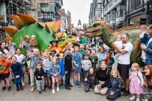 a group of adults and children having their photo taken with dinosaurs in chester city centre