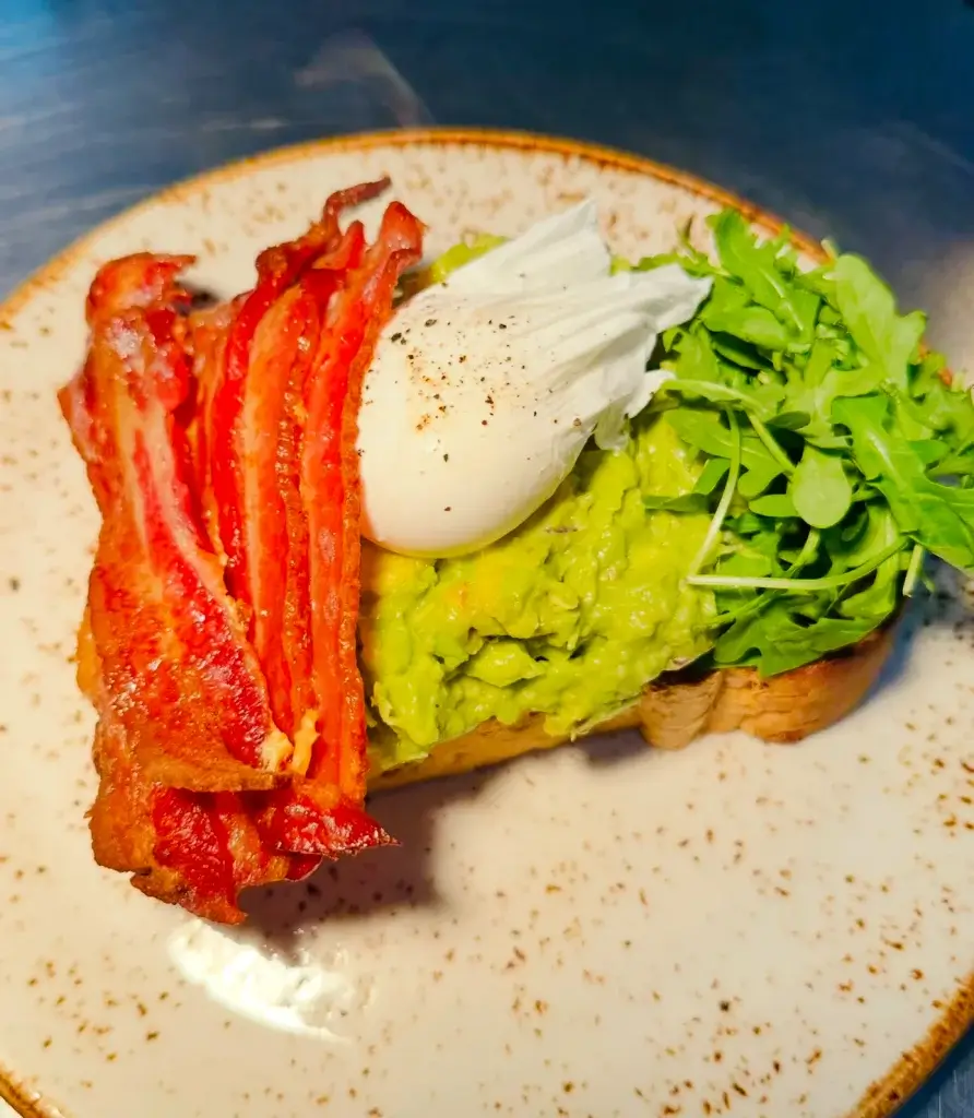 Eggs bacon and avocado on toast placed on a grey stone plate