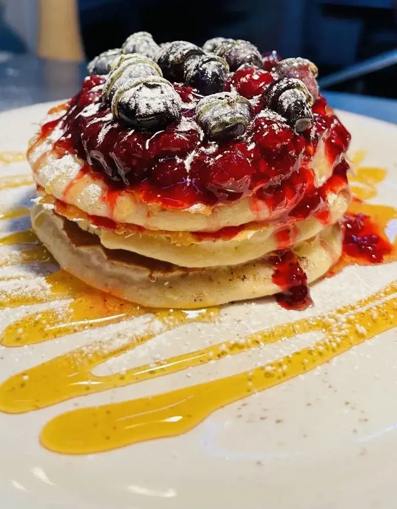 Blueberry placed on top of a stack of pancakes drizzled with caramel