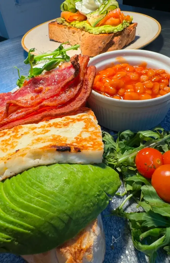 Eggs bacon and avocado on toast surrounded by other breakfast items