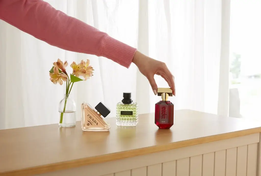 a selection of perfumes on a wooden topped table with a white curtain behind