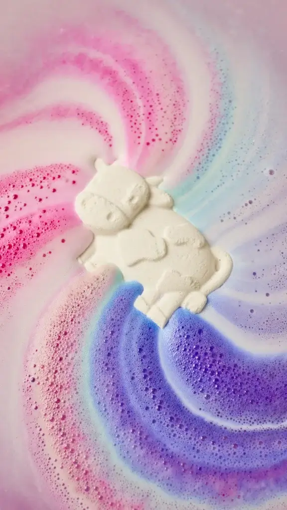 A bath bomb shaped like a cow in a rainbow coloured water