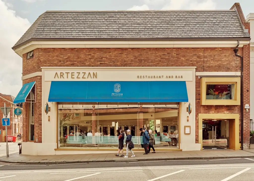 Exterior of Artezzan restaurant and bar, featuring a blue awning and large windows, with pedestrians walking by on a sunny day.