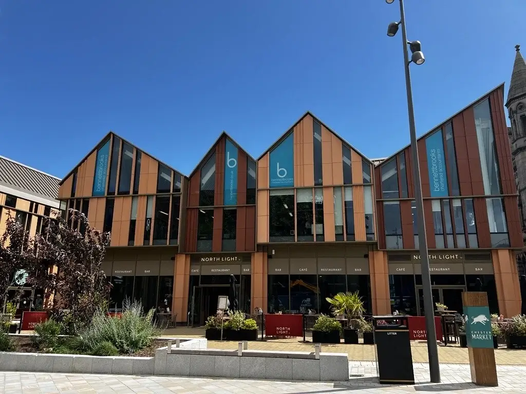 Modern building with wooden paneling, featuring "Bennett Books" signage, surrounded by greenery under a clear blue sky.