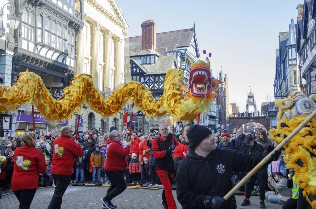 A Lunar New Year performance of people holding up a yellow dragon sculpture in front of Eastgate Clock