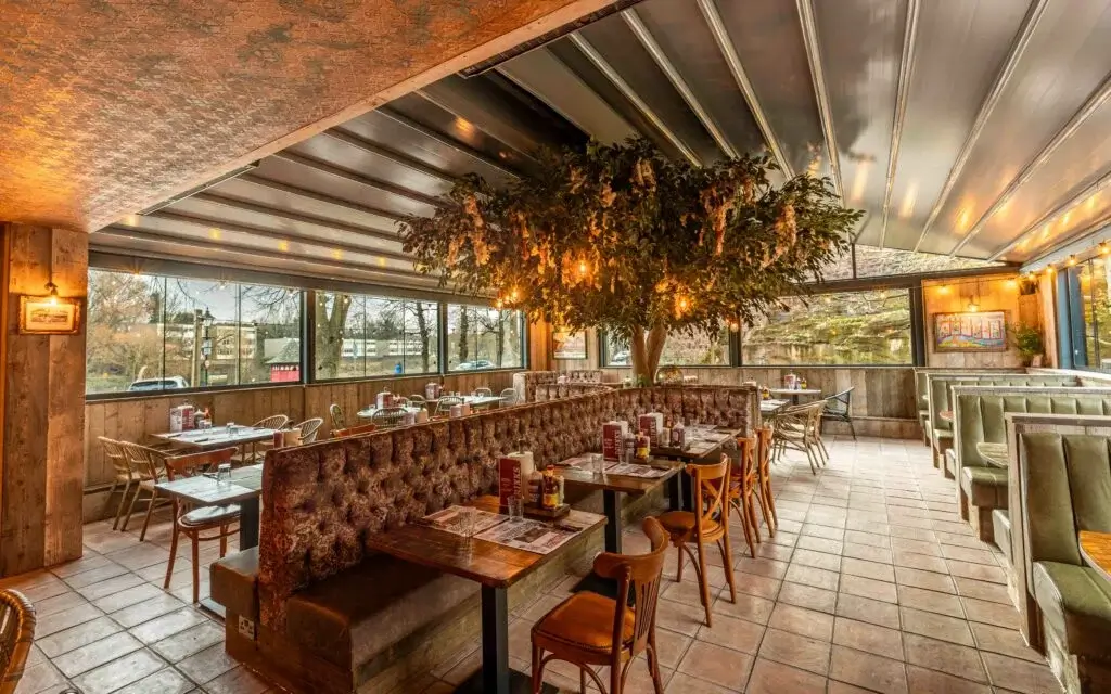 Modern restaurant interior featuring cozy seating, a large decorative tree, warm lighting, and tables set for dining.