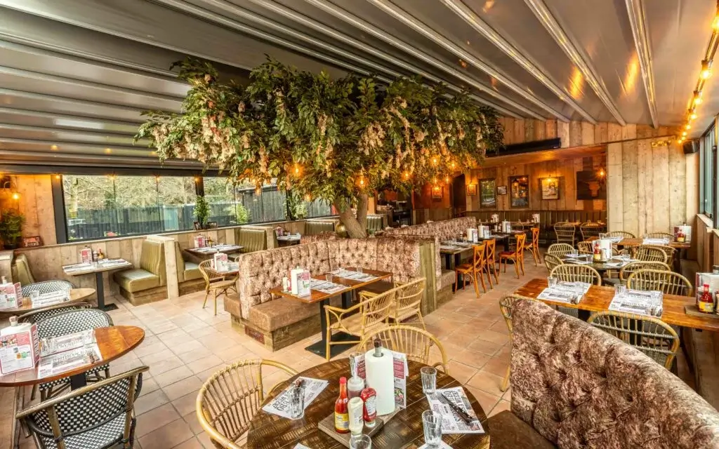 Modern restaurant interior featuring cozy seating, a large decorative tree, warm lighting, and tables set for dining.