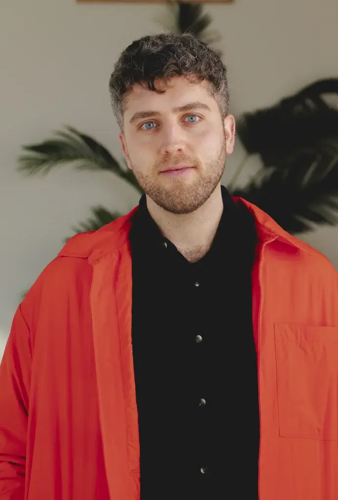 a man with facial hair wearing a black shirt and red jacket with blue eyes