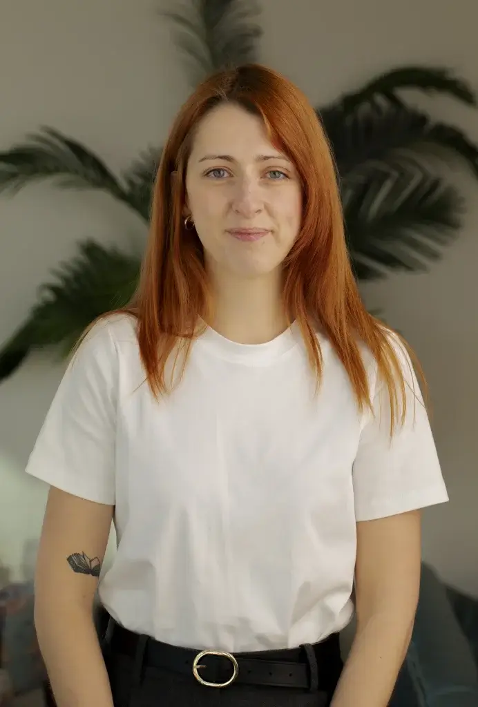 a woman with orange hair wearing a white top with a tattoo