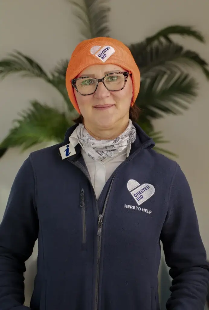 A woman in a purple jacket and orange hate with glasses