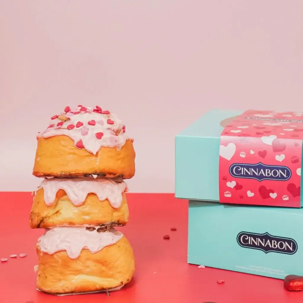 Cinnamon Buns with pink glazing sacked on top of one another on a pink table