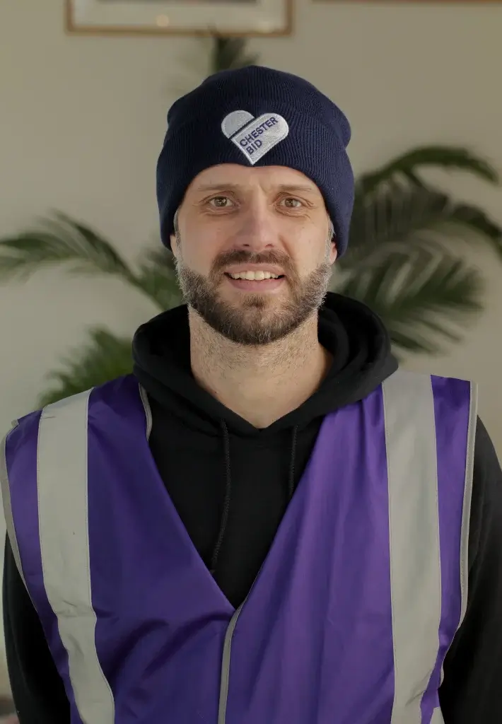 a white man with beard in a purple hate and purple high vis jacket