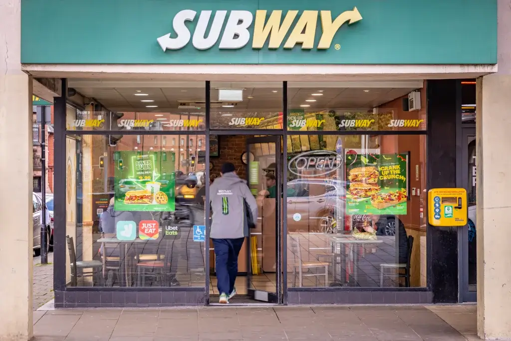 A Subway store with an open entrance, promotional posters, and outdoor seating, showcasing a welcoming atmosphere for diners.