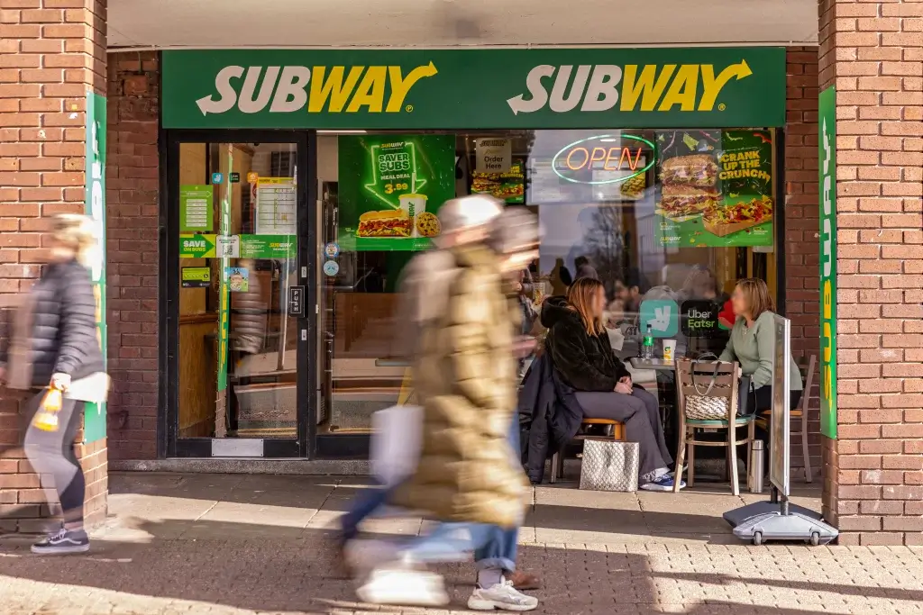 A Subway store with an open entrance, promotional posters, and outdoor seating, showcasing a welcoming atmosphere for diners.